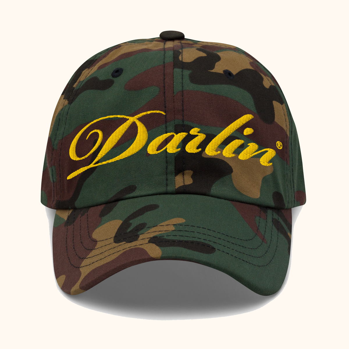 Front view of DARLIN® original script camouflage hat with yellow embroidery on a warm ivory background