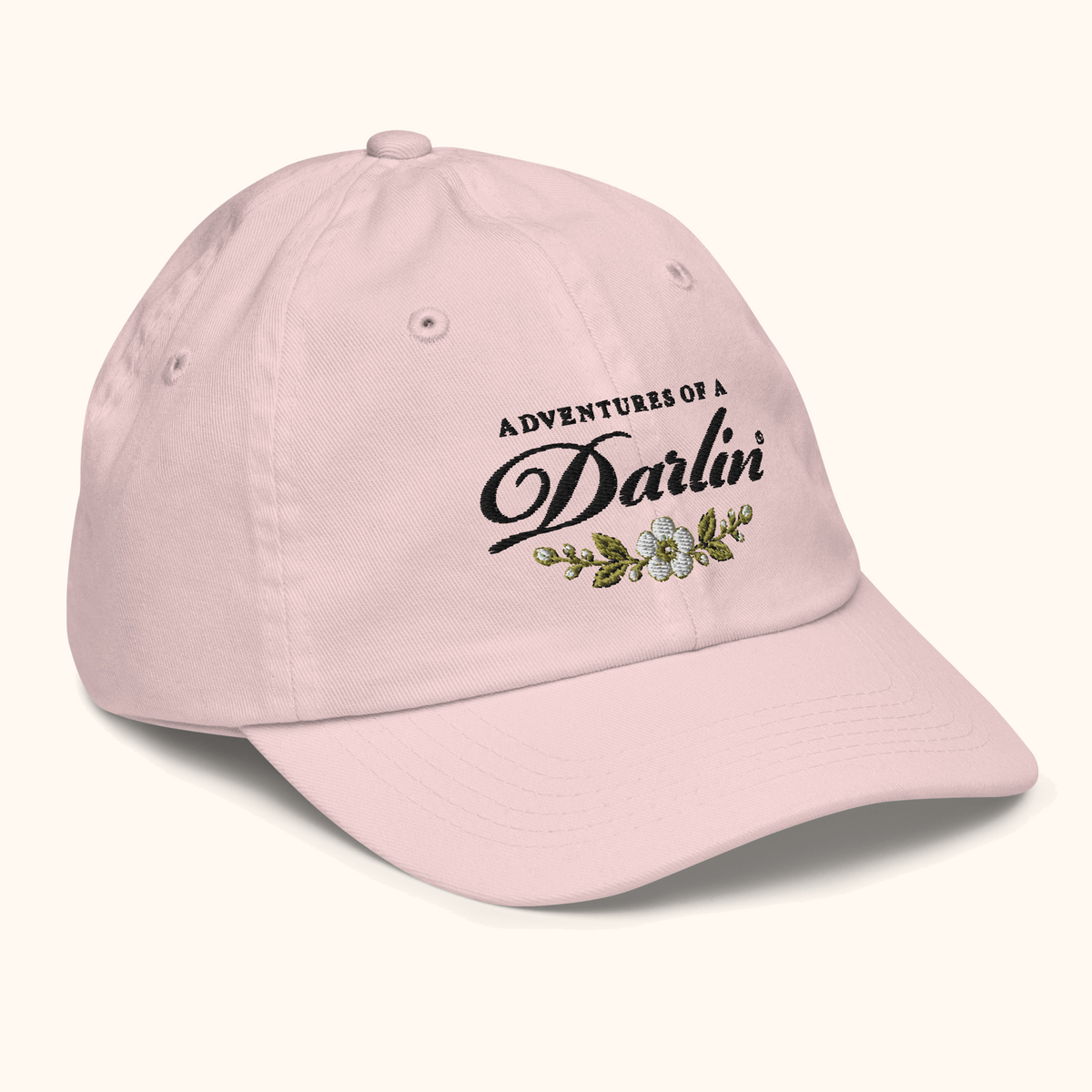 Angled view of the Adventures of a DARLIN® kids hat in vintage pink, showing the embroidered script, primrose floral detail, and curved brim.
