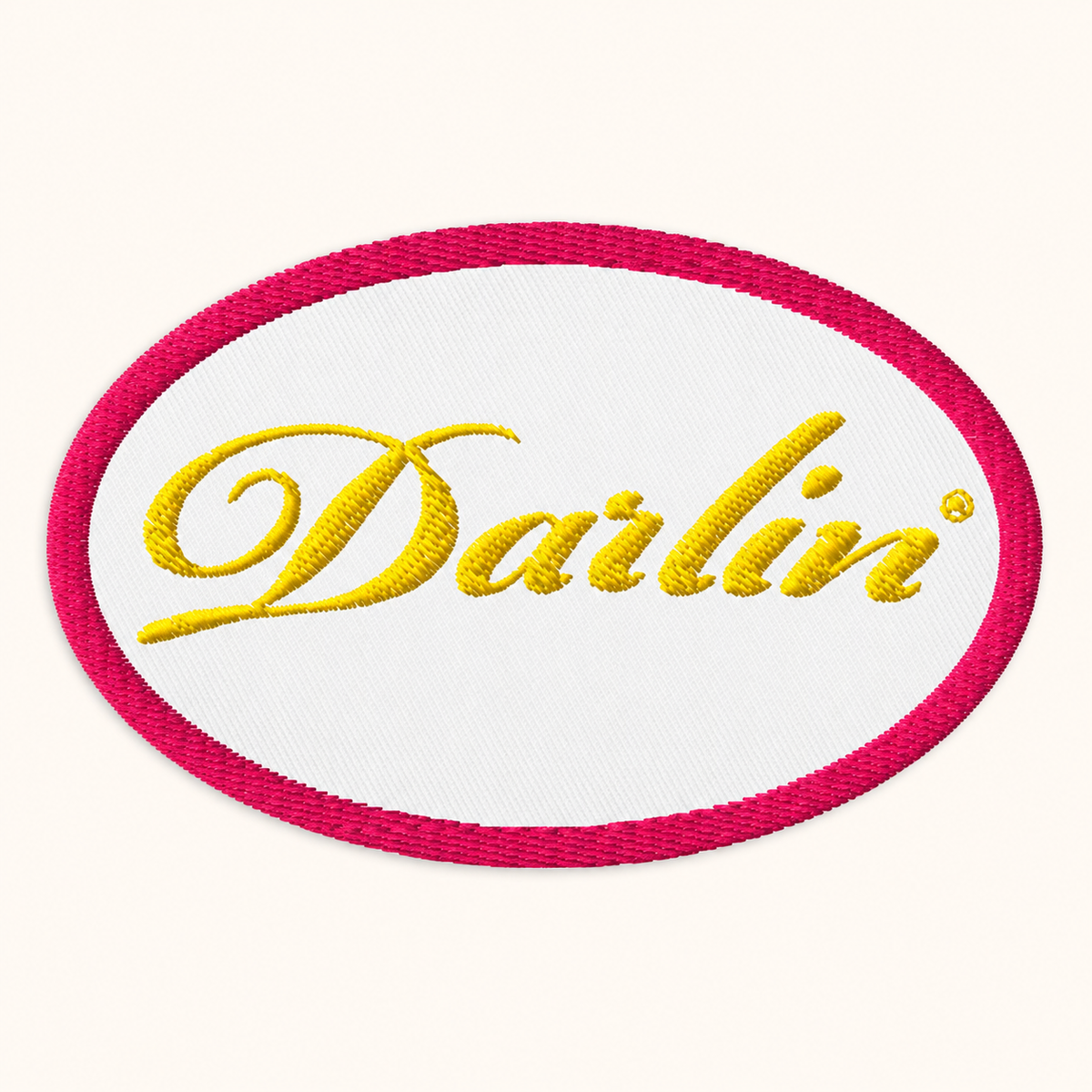 White oval DARLIN® embroidered patch with gold script lettering and a fuchsia stitched border, shown from the front.