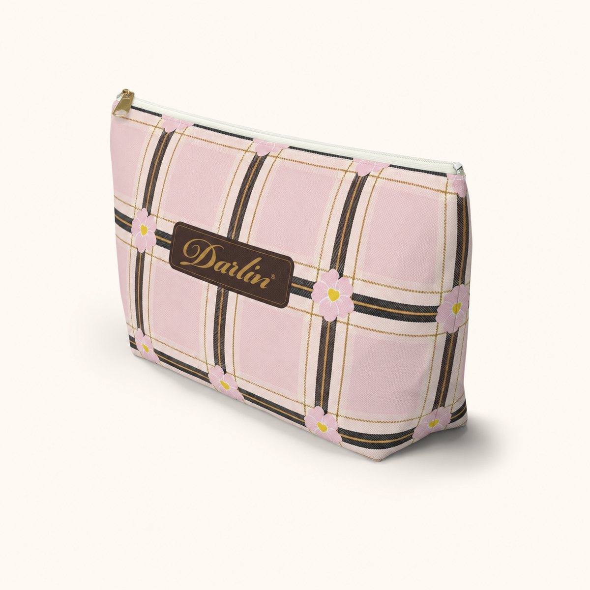 Angled view of the DARLIN® Primrose Plaid Travel Pouch showing its floral plaid, chocolate-and-gold registered script, zipper, and flat base.