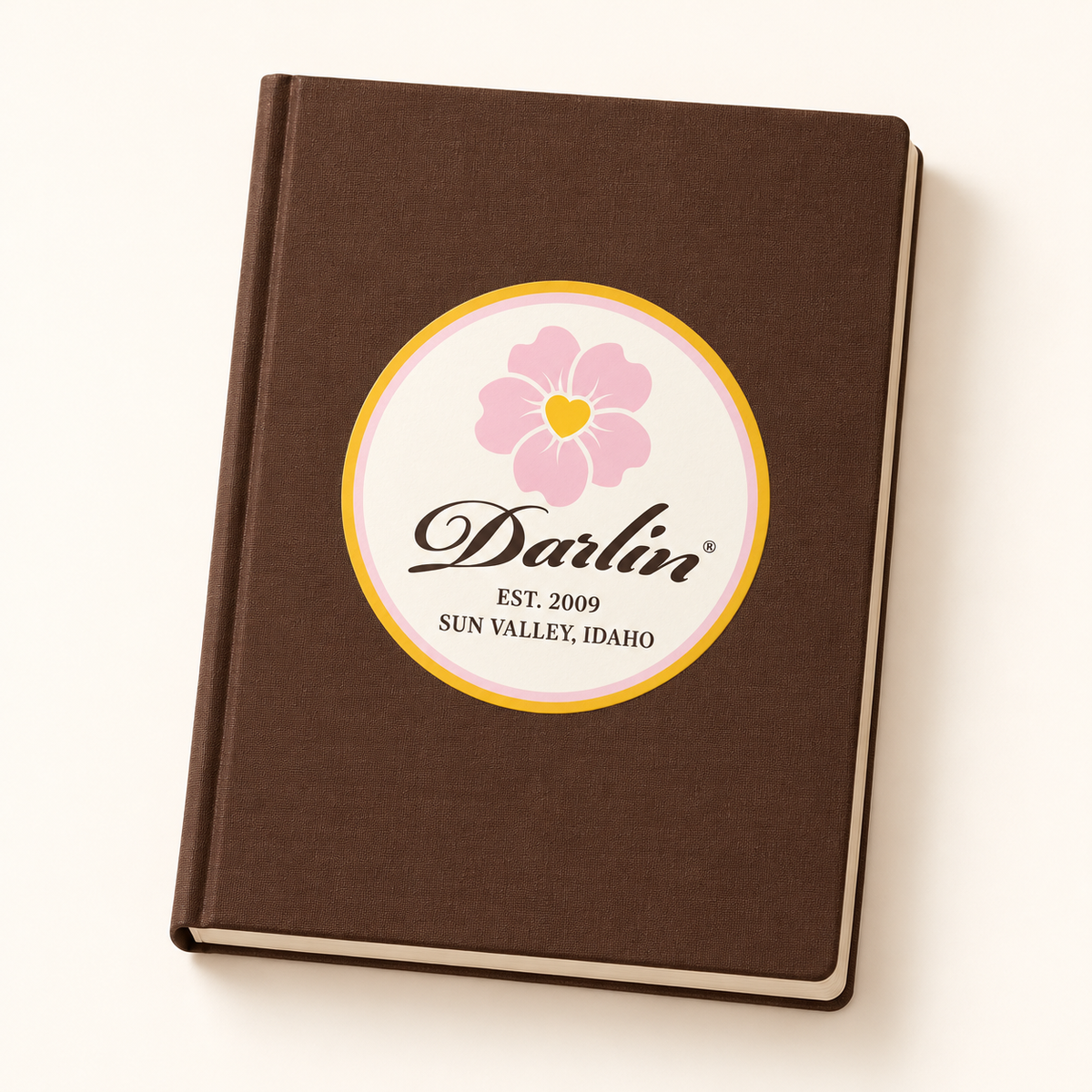 DARLIN® Script Heritage Sticker with a pink flower, chocolate script, and yellow border on a chocolate brown notebook.