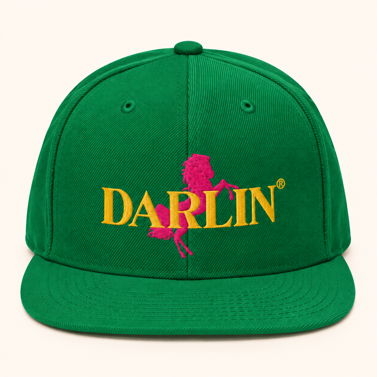 Green DARLIN® RIDE snapback hat with embroidered pink horse and gold DARLIN® logo on warm ivory background