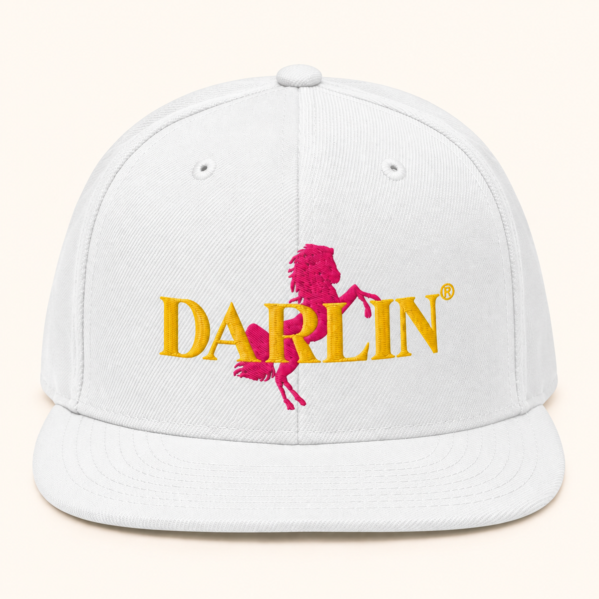 White DARLIN® RIDE snapback hat with embroidered pink horse and gold DARLIN® logo on warm ivory background