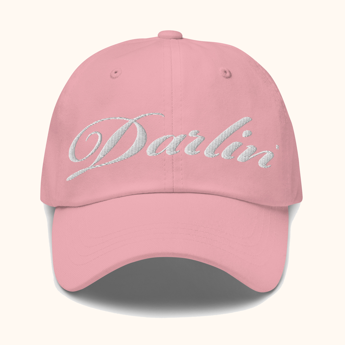 Front view of pink DARLIN® script hat with white embroidery on a warm ivory background