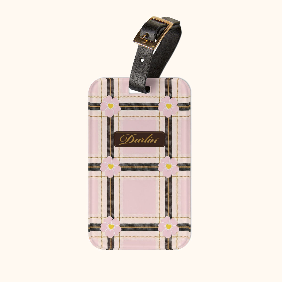 DARLIN® Primrose Plaid luggage tag with pink flowers, chocolate-and-gold script logo, and black strap on a warm ivory background.
